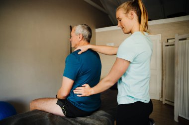 female physiotherapist performs back assessment for elderly man