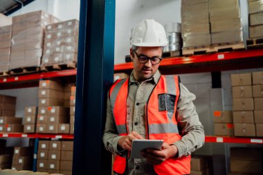 Male worker browsing on digital tablet wearing spectacles while standing in factory