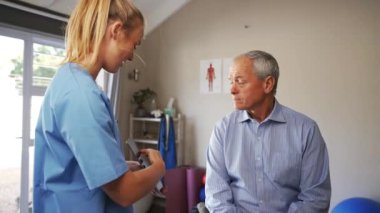 Female doctor in scrubs advising a elderly patient with digital tablet in hand, looking at results from medical test