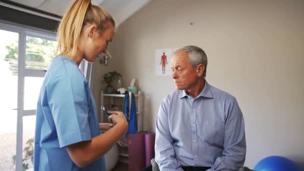 Tânăra femeie doctor în scrubs rezultatele discuțiilor cu pacienții vârstnici de sex masculin pe tabletă digitală — Videoclip de stoc