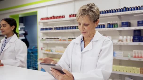 Caucasian female pharmacist wearing coat scrolling to find scripts on digital tablet in pharmacy — Stok video