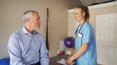 Caucasian female doctor in scrubs assessing elderly males shoulder mobility, ticking off check list