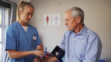 Caucasian female doctor in scrubs taking elderly male patients blood pressure in clinic