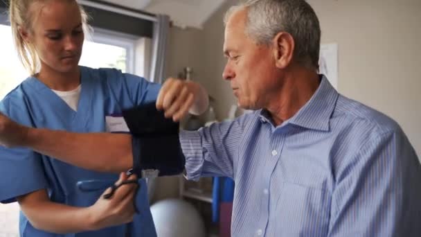 진료소에 앉아 있는 연로 한 환자의 혈압을 재는 여성 간호사. — 비디오