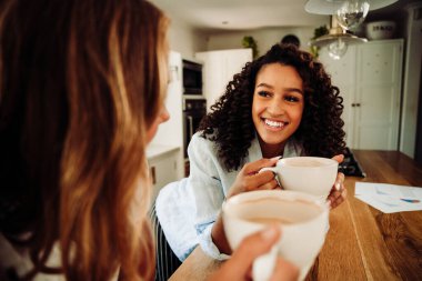 Mixed race friends laughing together in kitchen drinking hot coffee 