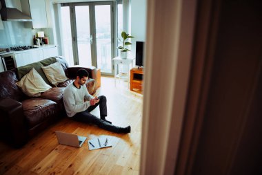 Mixed race business man sitting on lounge floor typing on cellular device working from home
