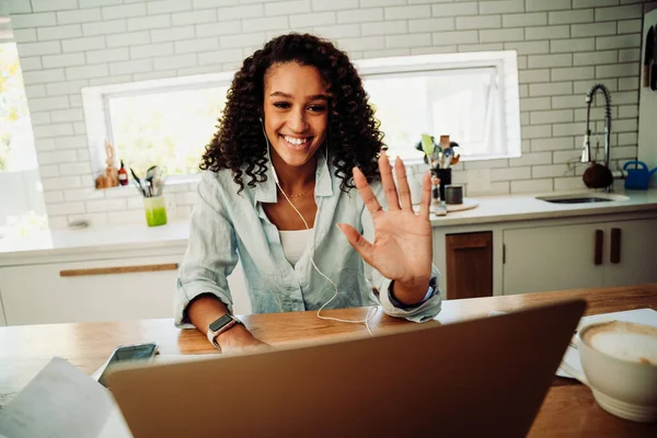 Mixed race female student waving on video call typing on laptop sitting in kitchen — ストック写真