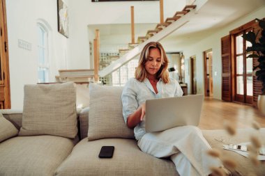 Caucasian female working from home sitting on couch typing on laptop