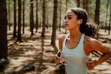 Mixed race female athlete running in forest listening to music with earphones
