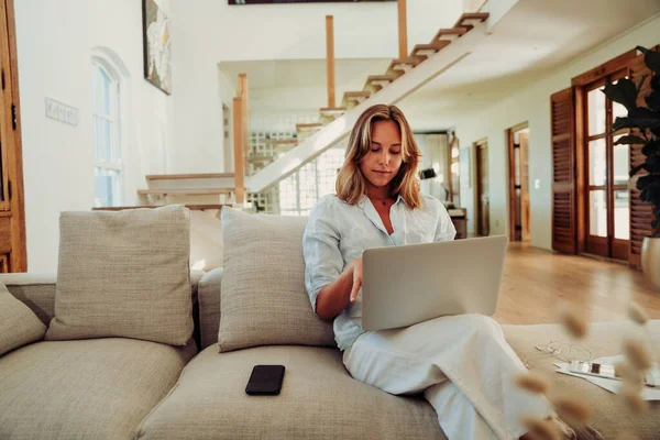 Caucasian female working from home sitting on couch typing on laptop — Fotografia de Stock