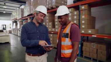 Fabrika deposunda elinde dijital tablet ve üniforma tutan çalışanı düzelten şık giyimli bir yönetici.