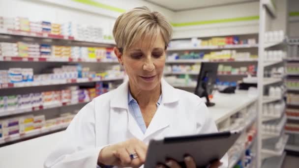 Seorang apoteker perempuan membaca email-email dari tablet digital sementara asisten mengatur obat-obatan — Stok Video
