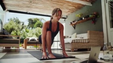 Beyaz kadın, spor salonunun kapısında gerinip laptopta video seyrediyor.