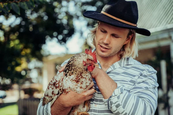 Caucasian male father petting pet chicken standing in farm village holding animal in hand