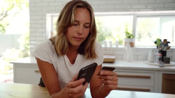 Blanke vrouw het maken van online betaling met mobiele apparaat glimlachen in de keuken — Stockvideo