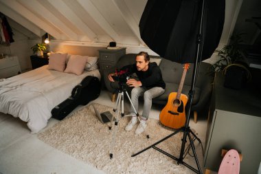 Genç erkek, video kamerayla şarkı kaydediyor. Konforlu müzik stüdyosunda gitar çalıyor.