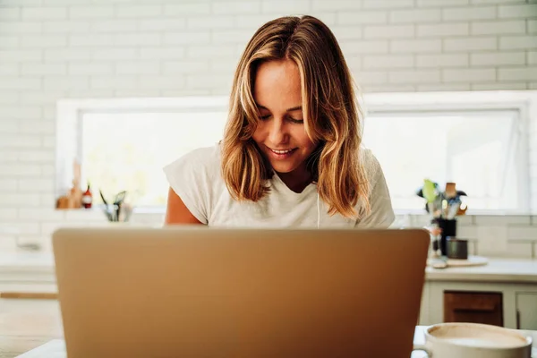 Caucasian female student working from home typing on laptop smiling in kitchen — 图库照片