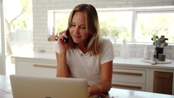 Blanke vrouw werken in de keuken chatten met vrienden op cellulaire apparaat typen op laptop — Stockvideo