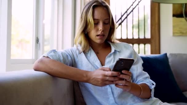 Blanke vrouw sms 'en op cellulaire apparaat zitten op de bank — Stockvideo
