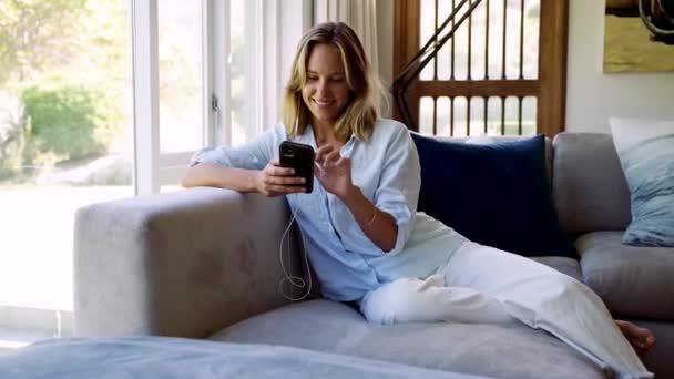 Mujer caucásica trabajando desde casa relajándose en el sofá escribiendo en el dispositivo celular — Vídeos de Stock