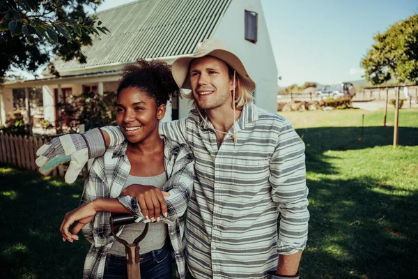 Verscheidene paar vrienden glimlachen in afstand tonen genegenheid staan in boerderij dorp in de voorkant van witte huis gekleed in tuingereedschap — Stockfoto