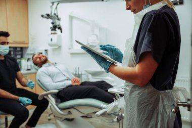 Beyaz kadın hemşire dijital tabletle yazarak erkek müşteriyle randevu prosedürünü belirliyor.