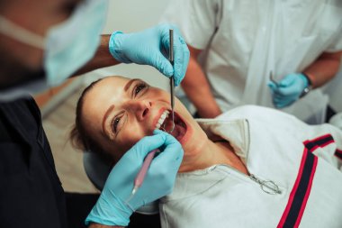 Erkek hemşire ameliyat ederken beyaz kadın ağzı açık yatıyor. 