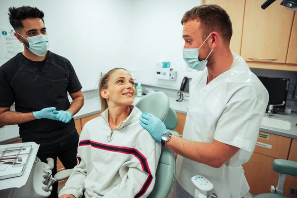 Caucasian smiling female lying on doctors bed while chatting to male nurses in doctors office