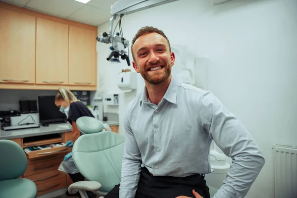 Handsome caucasian male standing in doctors office ready for appointment with female dentist — kuvapankkivalokuva