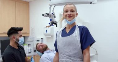 Klinikte kolları bağlı bir şekilde gülümseyen erkek müşterisiyle duran beyaz dişçi. 