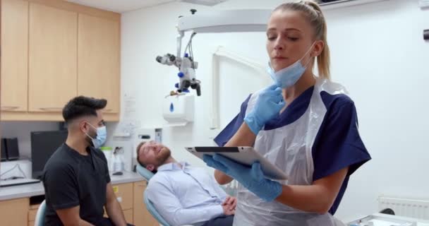 Caucasian female nurse wearing mask typing on digital tablet standing in doctors office — Stock videók