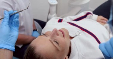Erkek hemşire dişlerini temizlerken beyaz kadın hasta doktor yatağına uzanıyor.