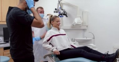 Erkek hemşire diş aletlerini taşırken beyaz kadın hasta doktor yatağında yatıyor.