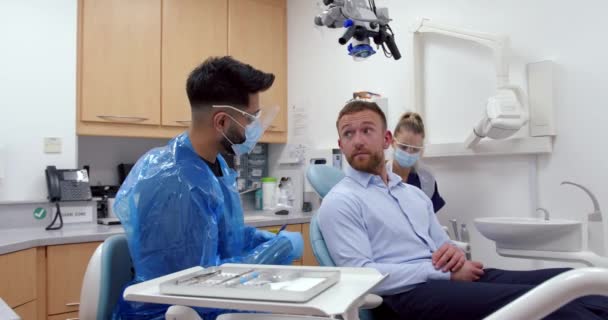 Caucasian male patient chatting to male nurse doctor lying on dentist chair before getting teeth cleaned — Stock Video