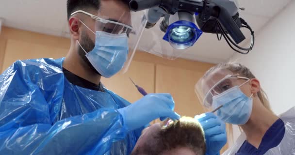 Белый мужчина-дантист чинит зуб пациенту мужского пола, сидящему в стоматологической палате — стоковое видео