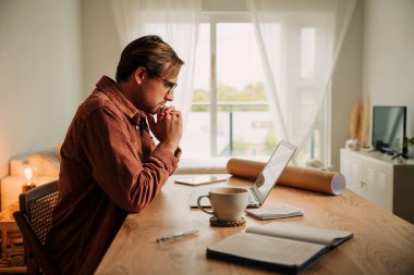Beyaz erkek iş adamı evde çalışıyor sıcak kahve içiyor video izlerken dinleniyor.