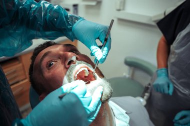 Hemşire dişlerini ameliyat ederken beyaz erkek müşteri dişçi koltuğunda oturuyor.