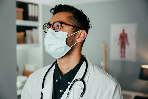 Médecin de race mixte travaillant à la clinique portant un masque chirurgical — Photo