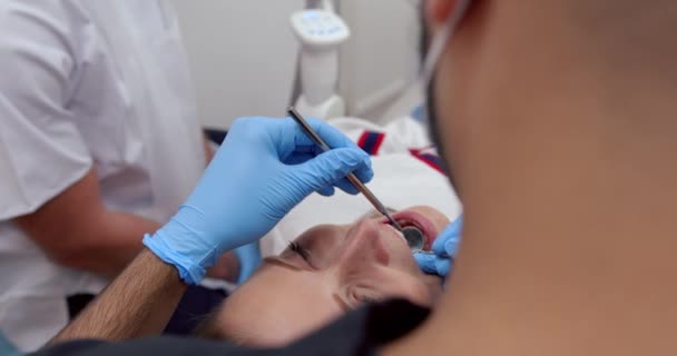 Femme blanche couchée dans le lit du dentiste tandis que l'infirmière masculine opère sur les dents avec des outils dentaires — Video