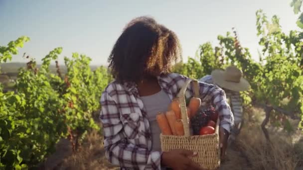 Mischlingshündin hält Gemüsekiste lächelnd in der Hand, während männlicher Partner hinter ihr gräbt — Stockvideo