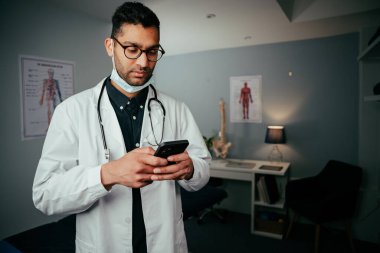 Karışık ırk erkek hemşire doktorların ofisinde cep telefonuna mesaj atıyor.