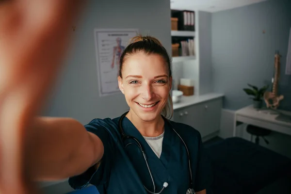 Καυκάσια γυναίκα γιατρός που παίρνει selfie στο γραφείο ιατρών με κυτταρική συσκευή — Φωτογραφία Αρχείου