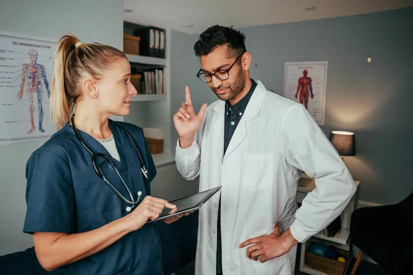 Λευκή γυναίκα νοσηλεύτρια ειδικευόμενη συνομιλεί με άνδρα γιατρό που στέκεται στο γραφείο κρατώντας ψηφιακή ταμπλέτα — Φωτογραφία Αρχείου