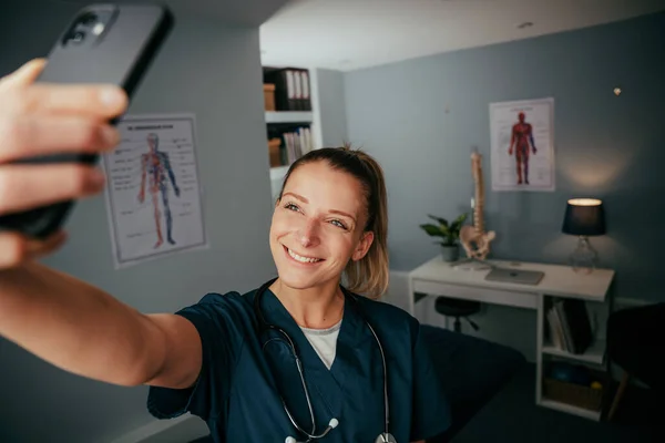 Blank vrouwelijke verpleegster staan in artsen kantoor het nemen van selfie op cellulaire apparaat — Stockfoto