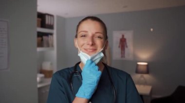 Cerrahi maske ve eldiven takan beyaz kadın hemşire doktorların ofisinde duruyor.