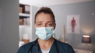 Cerrahi maske takan beyaz kadın hemşire doktorun ofisinde duruyor.