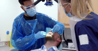 Erkek hemşire ameliyat ederken beyaz erkek hasta doktor yatağında yatıyor. 