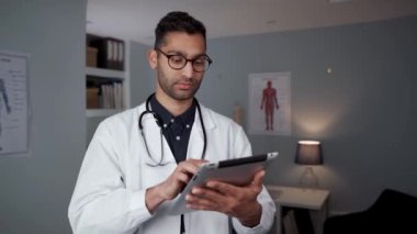 Doktor ofisinde dijital tablet üzerinde yazı yazan melez erkek doktor.