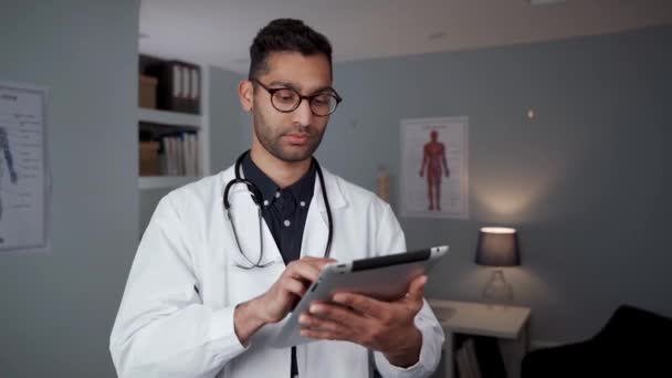 Μικτή φυλή αρσενικό γιατρό δακτυλογράφηση σε ψηφιακή δισκίο στέκεται στο γραφείο γιατρούς — Αρχείο Βίντεο