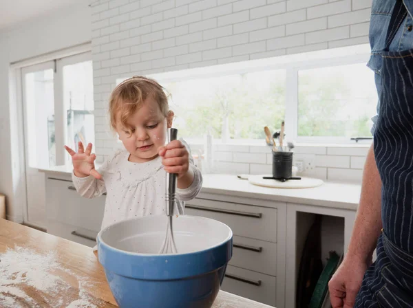 Menina bebê batendo em uma tigela de mistura na cozinha com o pai — Fotografia de Stock